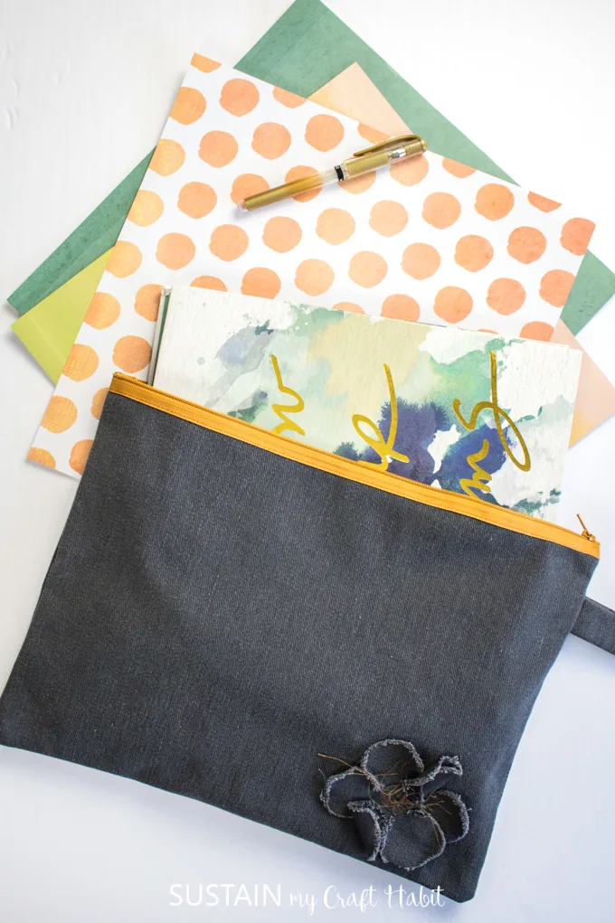 A notebook and decorative paper spilling out of the finished oversized pencil case made from this how to sew a pencil case with a zipper tutorial.