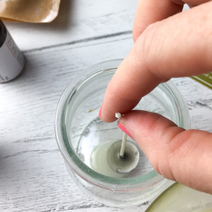 Placing the candle wick into the bottom of the glass jar.