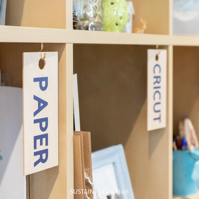 Wooden organization labels hanging in cubby's to identify craft supplies in a craft room.