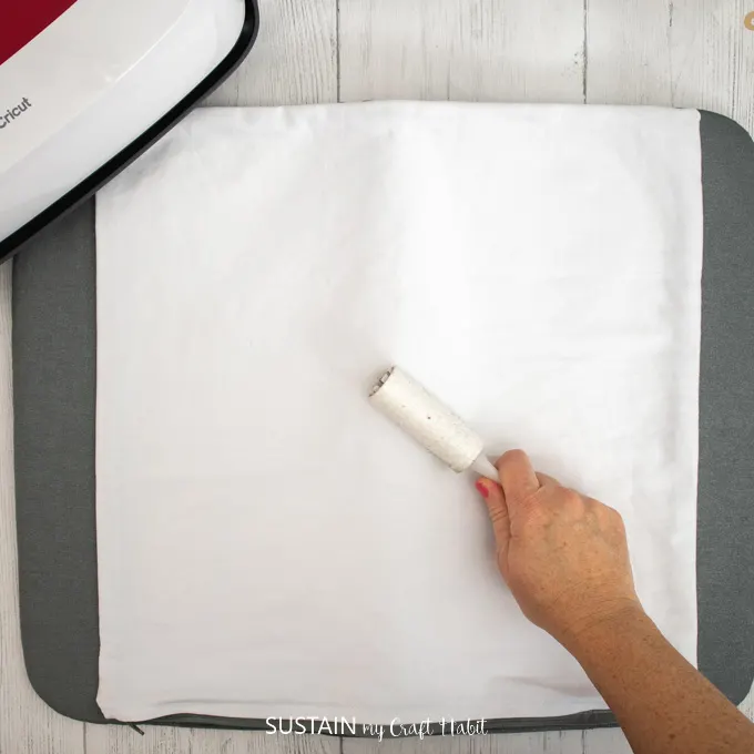 Using a small lint roller to remove lint from pillow cover before applying the adhesive vinyl.