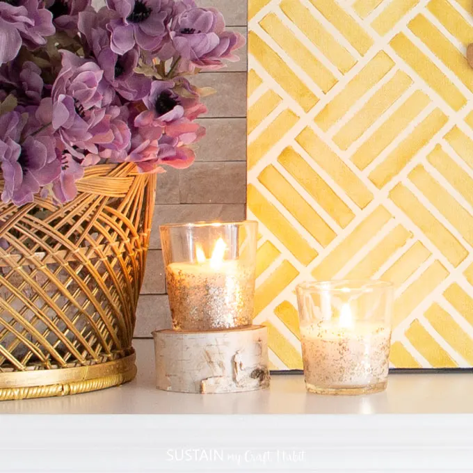 Two glass votive candles burning on the autumn fireplace mantle.