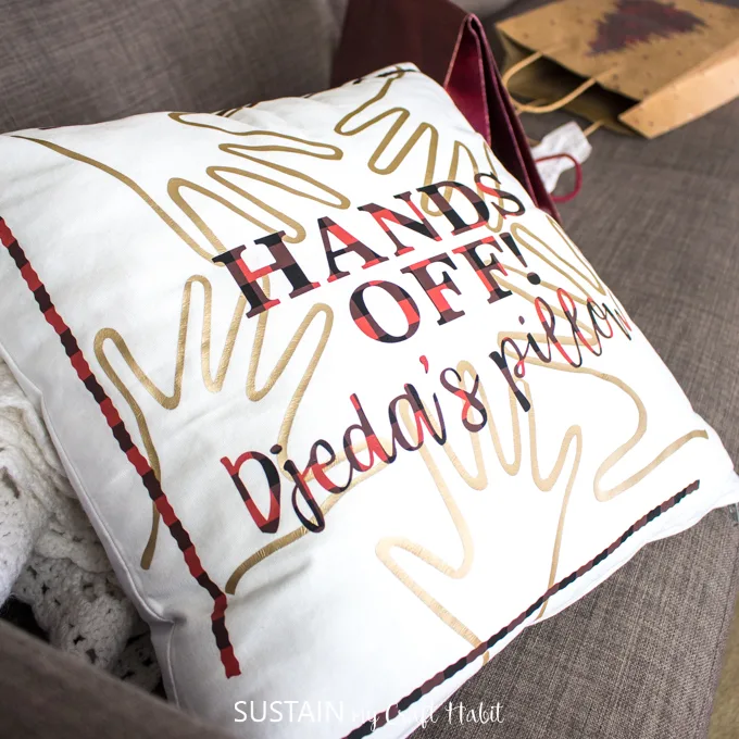 Close up view of "Hands off! Djeda's pillow" on a couch surrounded by opening gift bags.