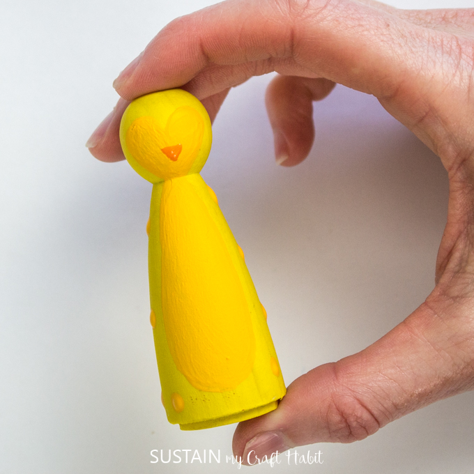 Nearly finished details of a yellow penguin painted on a wooden peg.