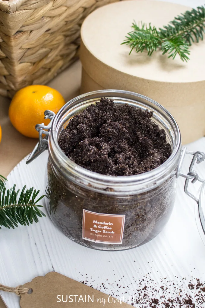 DIY sugar scrub make with coffee grounds and essential oils in a small jar surrounded by natural elements.