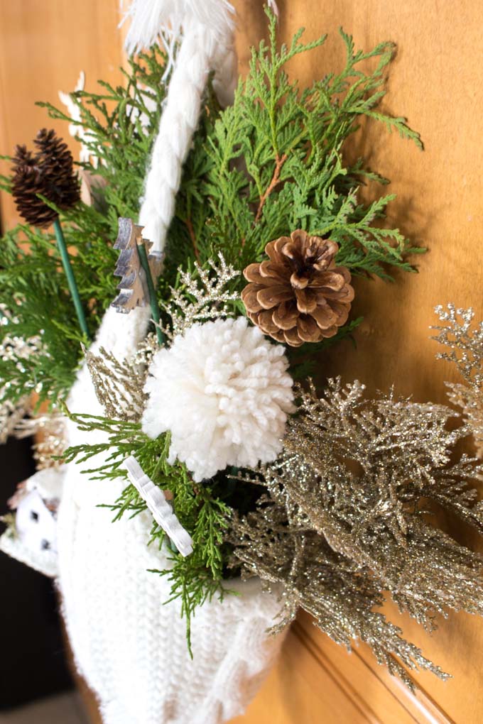 Close up of white winter hat with decorative pics, such as gold branches, pom pom and a pine cone.