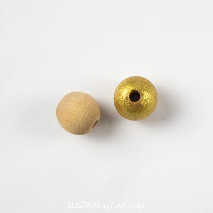 Two wooden beads with one wood bead painted gold.