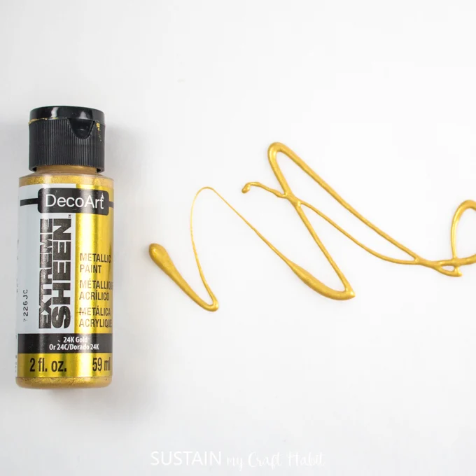 Paint container with gold paint drizzled over parchment paper