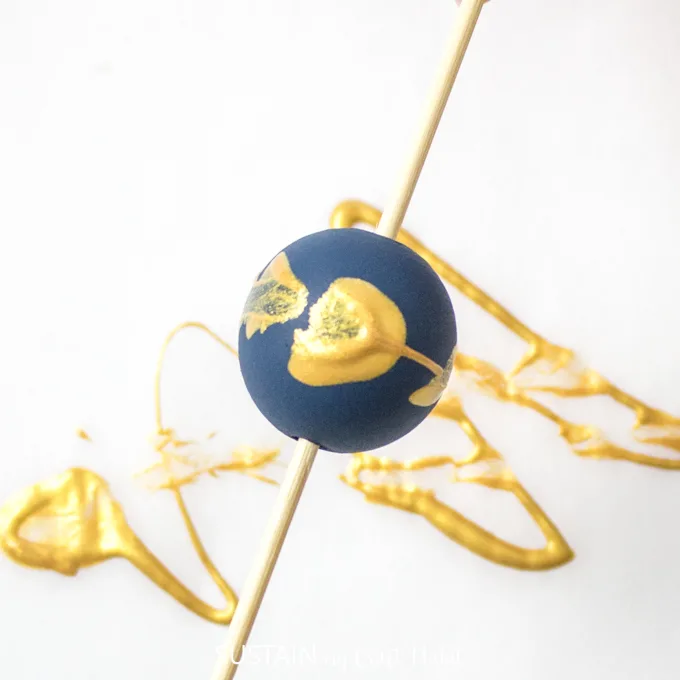 Close up of blue painted wood bead with gold splatter