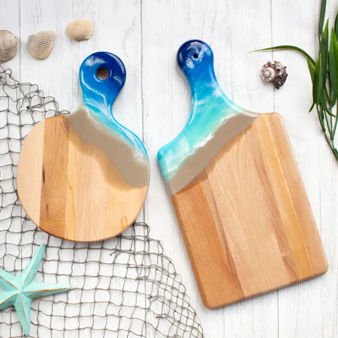 Two wooden cutting boards with resin handles resembling the seashore.