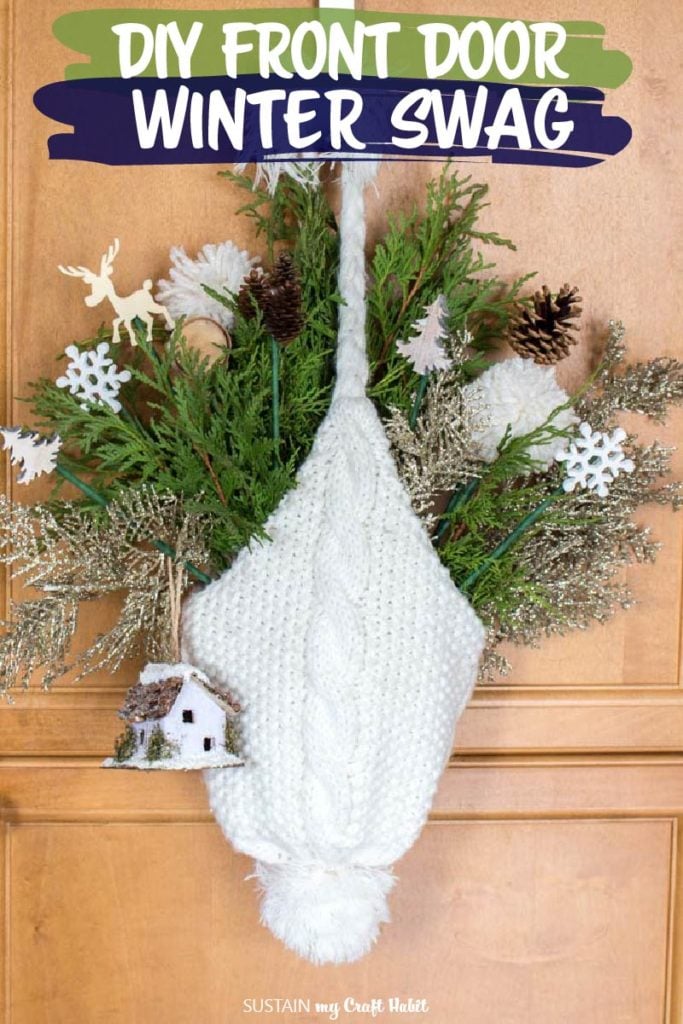 A white winter hat hanging from a hook. The hat is filled with greenery and small decorative picks such as a snowflakes, trees, pine cones, wood slices and a birdhouse.
