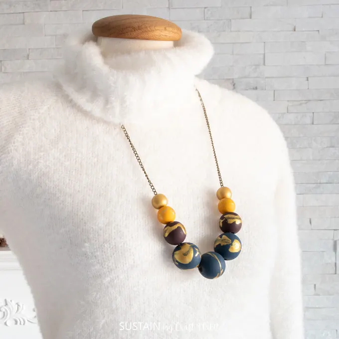 Necklace with painted wood beads on gold chain placed over mannequin with a white sweater.