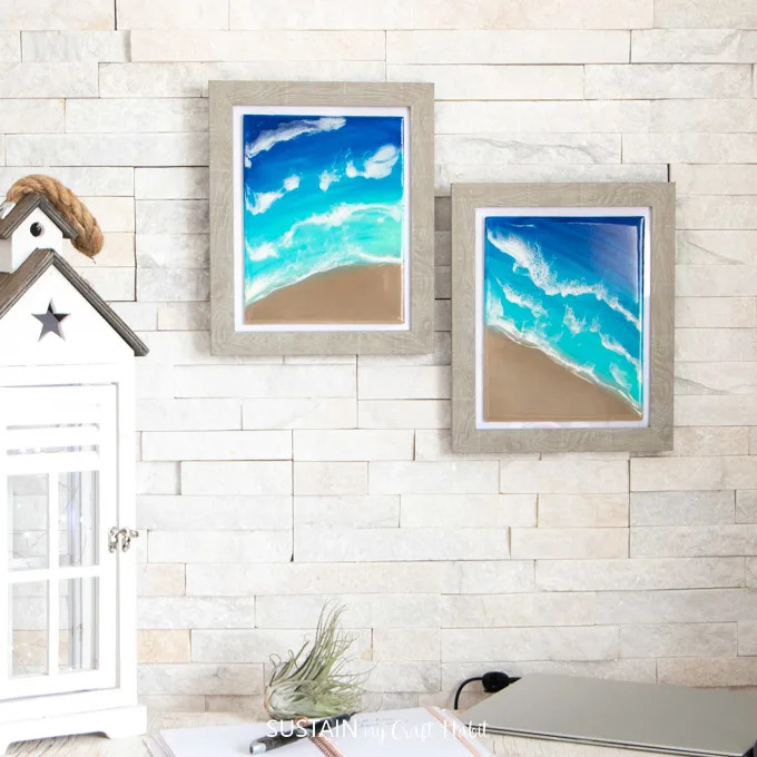 Two framed beach resin artwork pieces hung on a wall above an office desk.