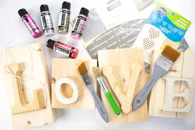 Craft materials that include wooden blocks with letters l,o,v,e, paint brushes, stencils and paint