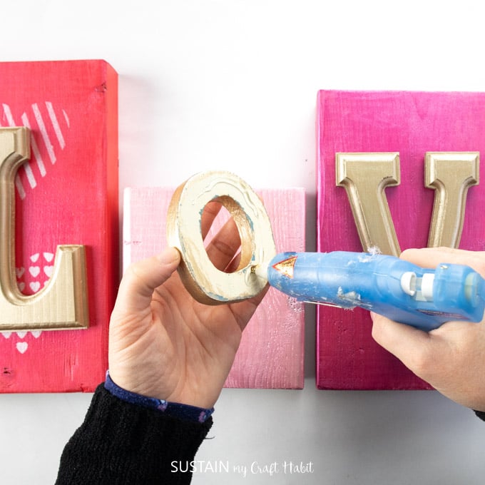 Gluing the gold painted letter O onto a pink painted wooden block.