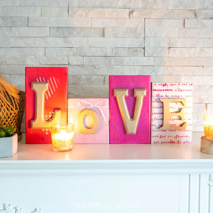 Colorful wood blocks with gold letters that spell out "love". They're sitting on a mantel behind a lit candle.