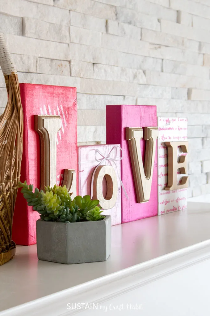Colorful wood blocks with gold letters that spell out "love". They're sitting on a mantel behind a green succulent plant.