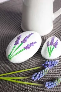 Oval rocks painted white with a purple grape hyacinth flower design.