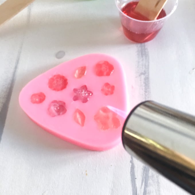Using a small kitchen torch to blow off bubbles from the top of the resin molds in the pink silicone mold.
