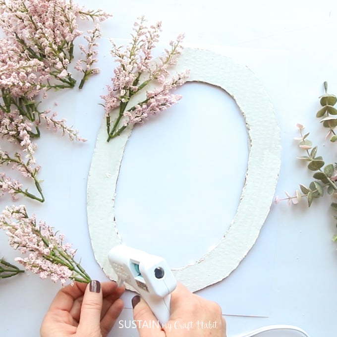 Using a hot glue gun to glue flowers onto the white painted cardboard letter O.