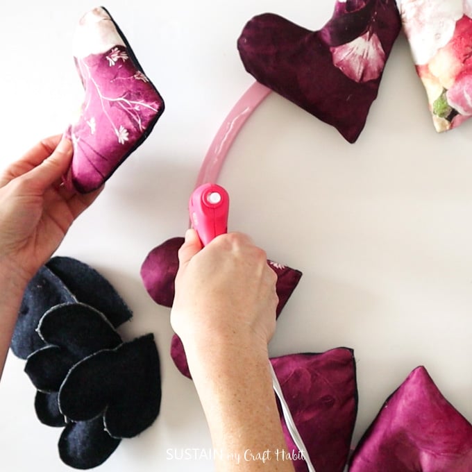 Using a hot glue gun to glue the finished fabric hearts onto the painted pink hoop ring.