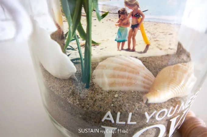 Close up of the sand, sea shells and picture inside the glass jar.