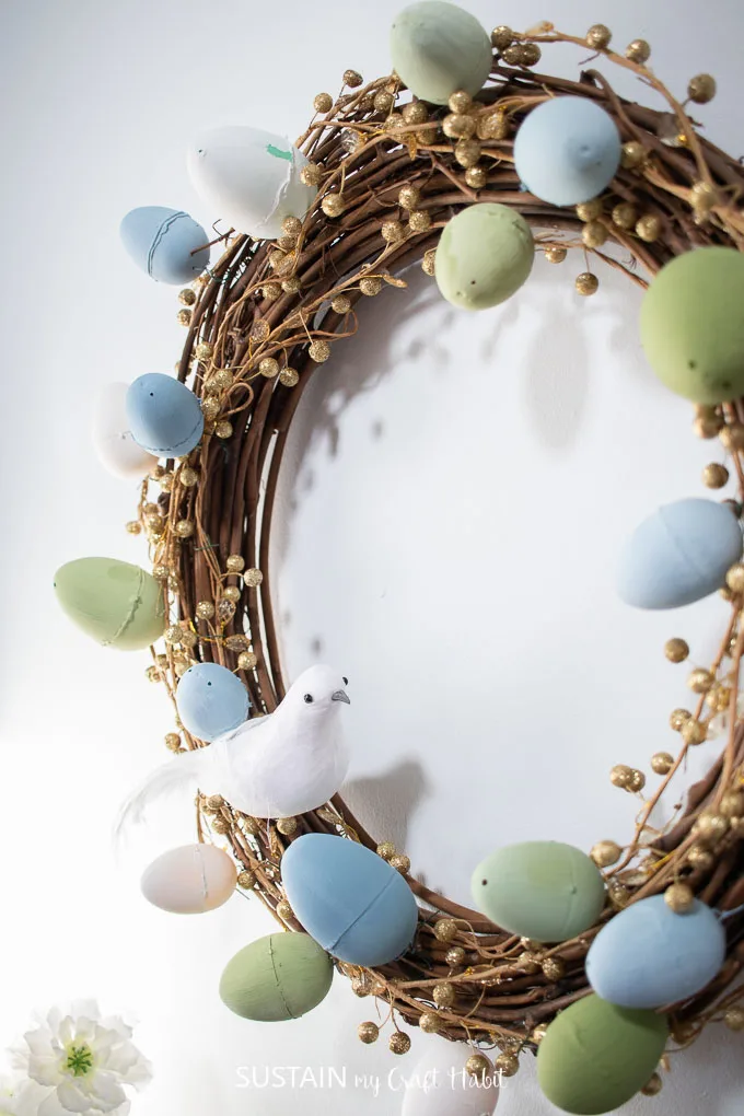 Close up of finished Easter wreath with gold garland, painted Easter eggs and a decorative bird.