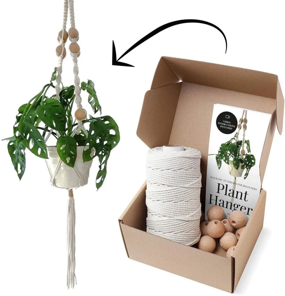 A potted monstera plant in a completed macrame plant hanger. A cardboard box with the materials and instructions to make the planter.