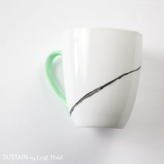 Adding a diagonal line with black paint on a white mug.
