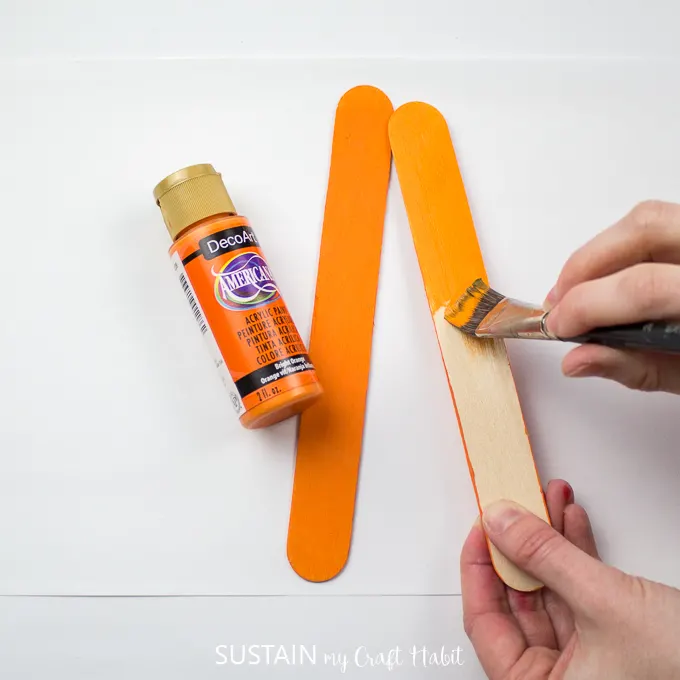 Painting a wooden popsicle stick in DecoArt orange color.