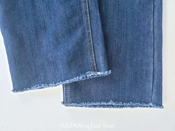 A pair of demin pants with a frayed edge hem.