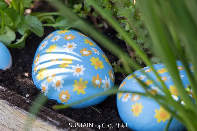 Close up of flower painted rocks sitting in a garden bed.