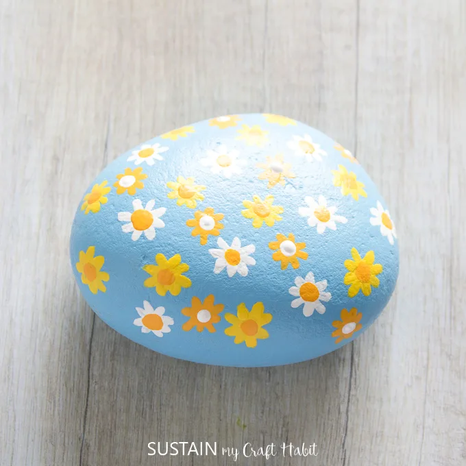 Finished daisy flowers painted on a blue rock.