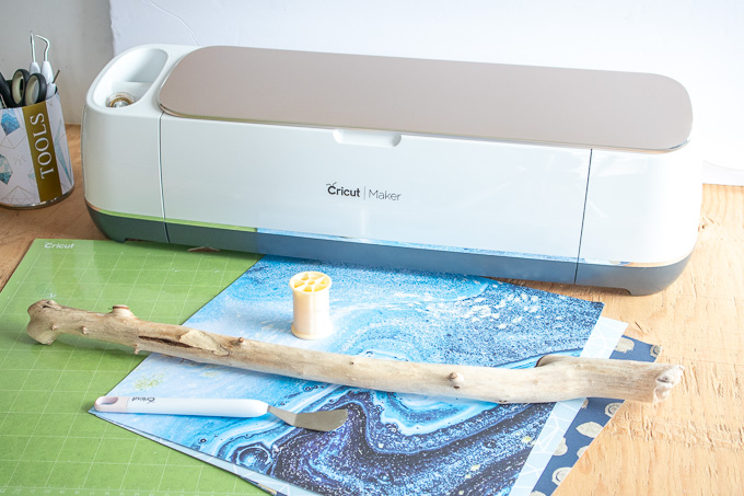 Blue and teal decorative papers in front of a Cricut Maker machine on a wooden surface.