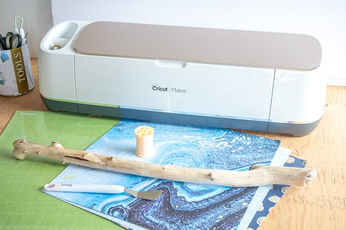 Blue and teal decorative papers in front of a Cricut Maker machine on a wooden surface.