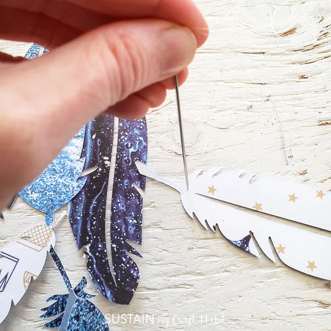 Using a sewing needle to poke a hole through a paper feather.