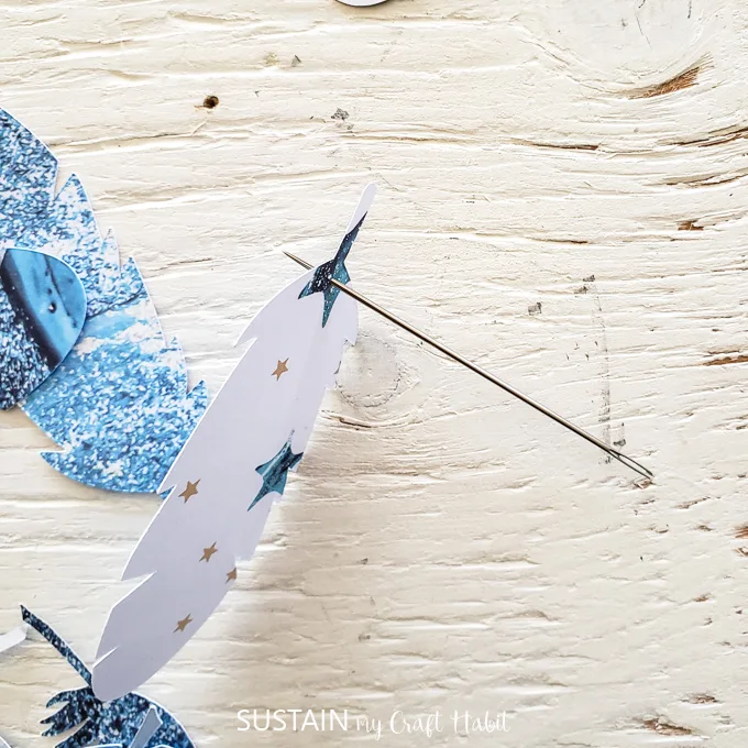 Using a sewing needle to poke a hole in the top of a paper feather.