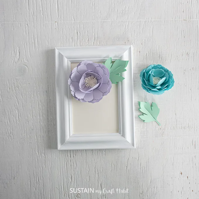 Arranging the purple peony and green leaf onto the white picture frame.