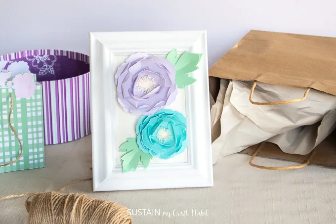 Purple and teal paper peonies in a white photo frame.