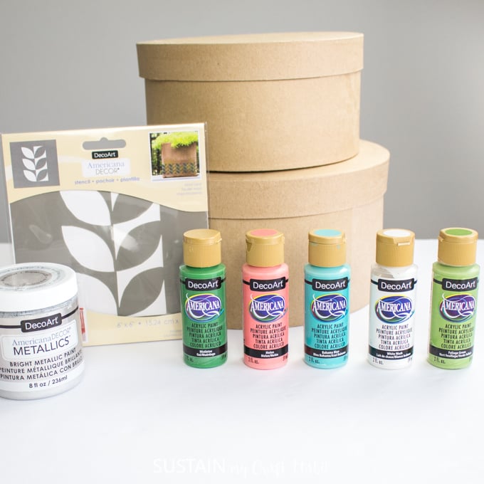 Materials needed to paint the modern retro craft hat boxes, including two hat boxes, paints, and a leaf stencil.