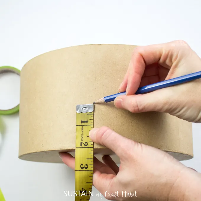 Using a measuring tape to measure 2" from the bottom of the craft hat box and using a pencil to mark the spot.