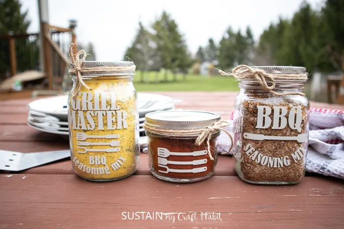 Finished labeled mason jars which are filled with BBQ seasoning and tied with twine, sitting on top of a picnic table as a Father's Day BBQ gift idea