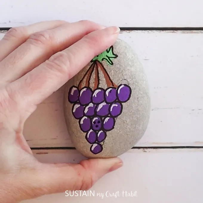 Holding a rock to show the painted grapes and smiley face.