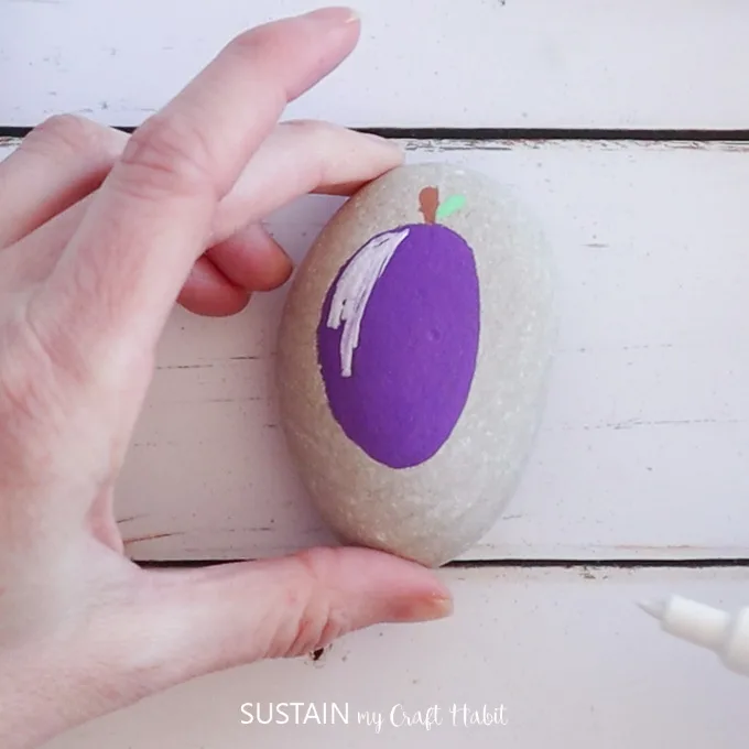 Adding a stem, green leaves and highlight on a plum painted rock.