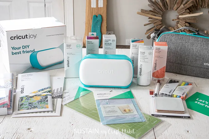 The new Cricut Joy cutting machine along with a variety of accessories and materials arranged on a white wood table.