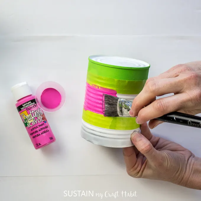 Painting the middle of a tin can with pink paint.