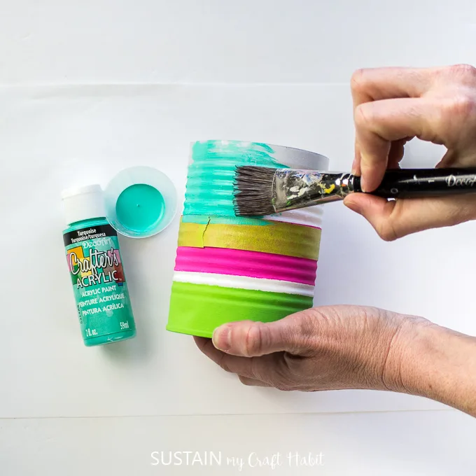 Painting the bottom of the tin can with turquoise paint.