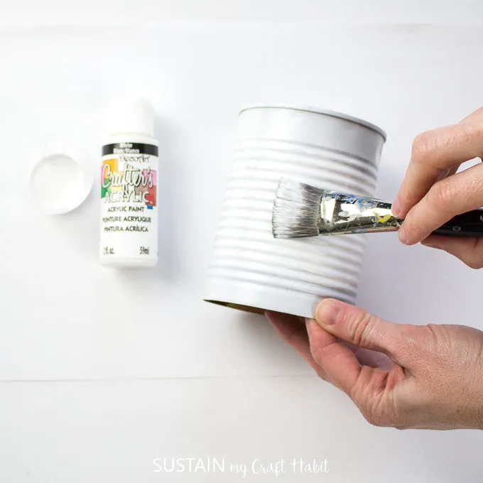 Painting the middle of a tin can with white paint.