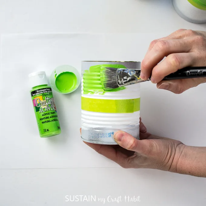 Painting the top of the tin can with green paint.