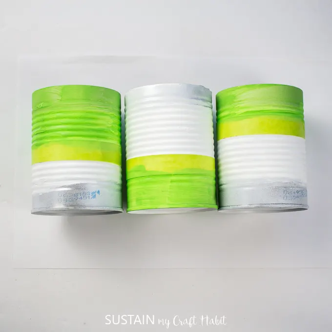 Three tin cans painted in different spots with green paint.