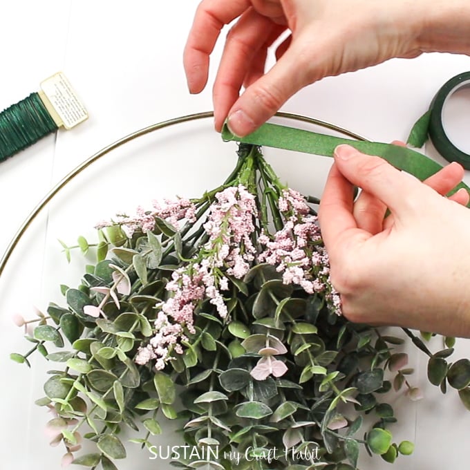 Using floral tape to cover the floral wire and stems of the eucalyptus plants and floral bunches.